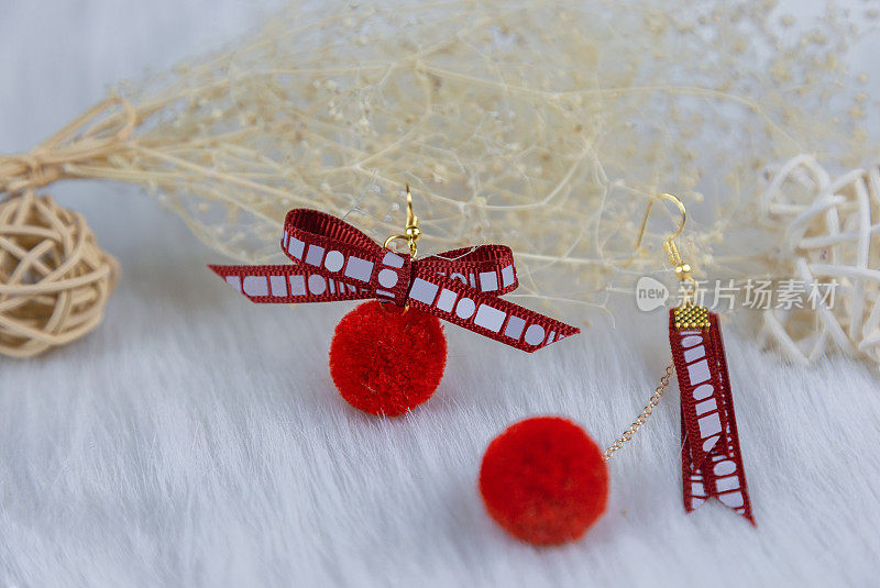 红色的绒球耳环，它的形状是一个毛茸茸的球。耳环旁边有一些装饰物，如sepak takraw和花束标本。这些东西都放在薄纱上。耳环看起来非常优雅和时尚。